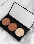 Photo de la palette de contouring en poudre ARTIST. À la droite se retrouve la teinte brun froid, au centre le brun chaud et à la droite le beige clair. Le tout dans un boîtier noir avec un miroir.